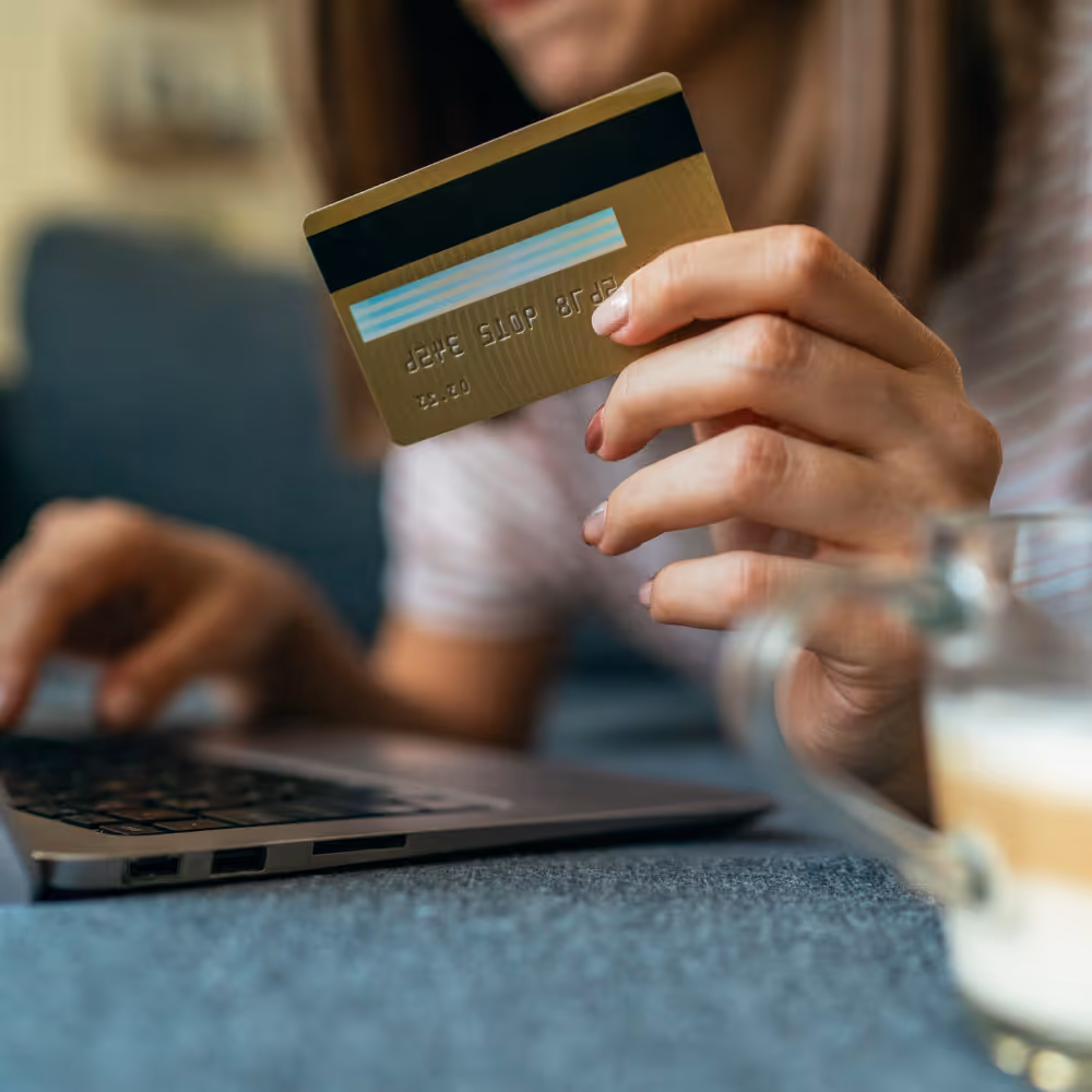 Person holding a credit card in one hand while typing on a laptop with the other hand.